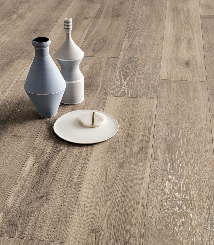 Wood-effect porcelain stoneware flooring in a natural tone, with realistic grain patterns and decorative ceramic objects.