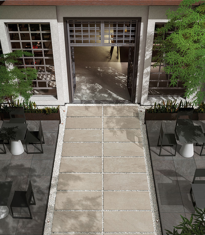 Contemporary outdoor space with stone-effect porcelain stoneware flooring, large slabs laid on gravel, essential furnishings and integrated greenery.