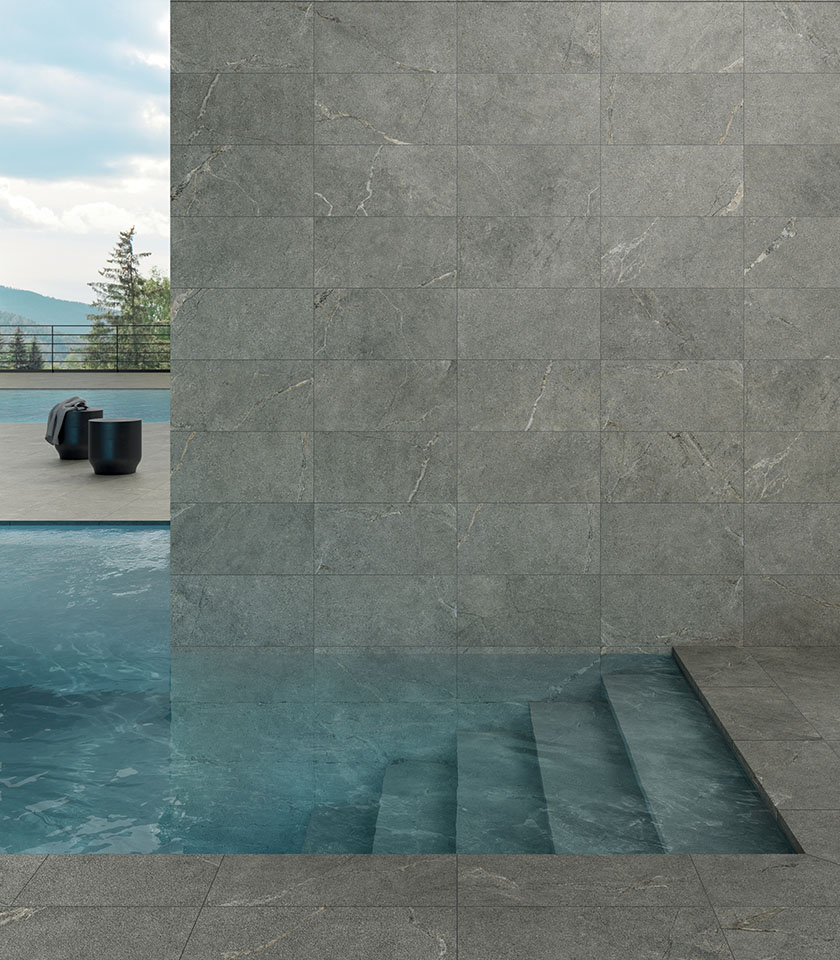 Swimming pool with grey stone-effect porcelain stoneware wall and floor tiles, submerged steps and mountain views.