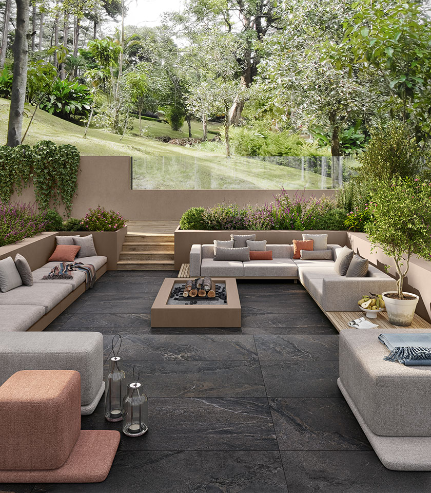 Terrace surrounded by greenery with dark stone-effect outdoor flooring, spacious lounge seating and integrated planters for an elegant and welcoming setting.