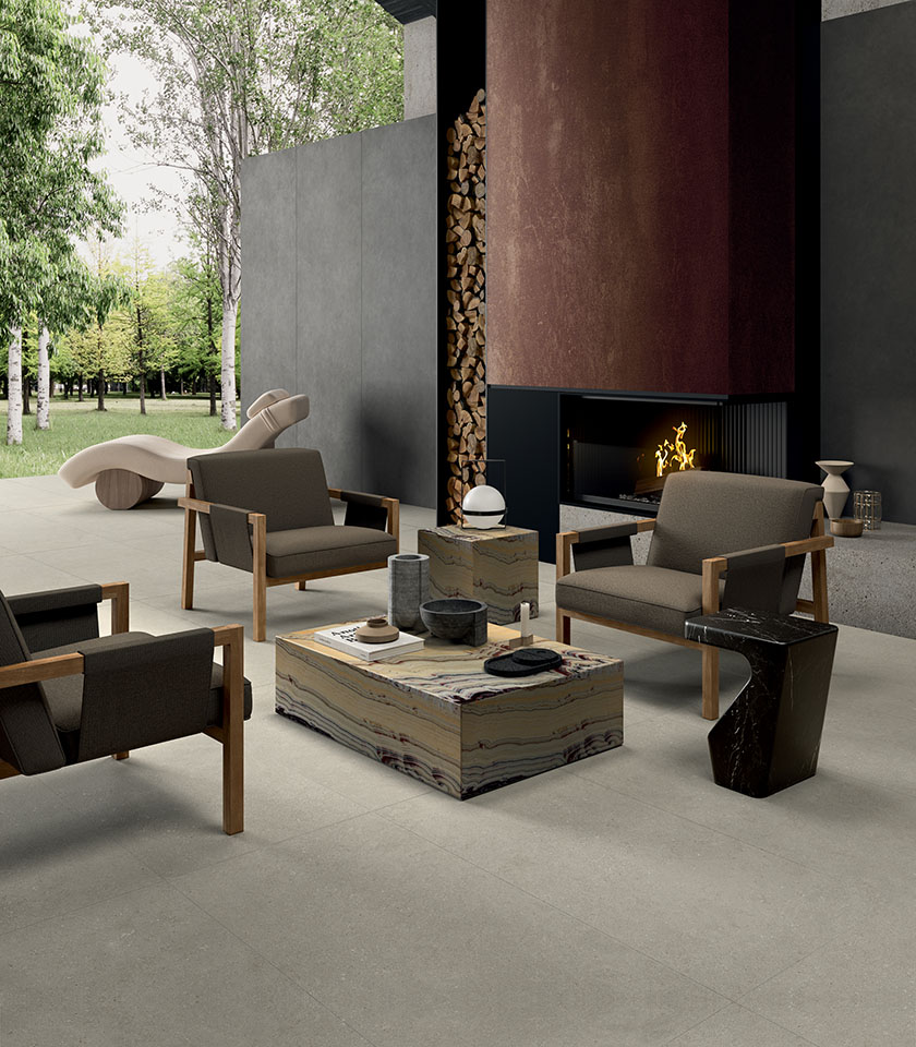Contemporary outdoor space with light porcelain stoneware flooring, a lounge area with fireplace, designer furniture and views of the surrounding greenery.