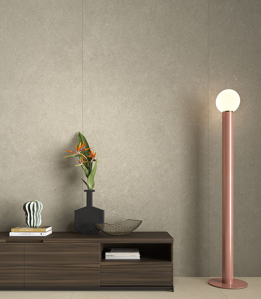 Contemporary interior with large-format concrete-effect wall tiles, a low wooden cabinet and a decorative floor lamp.