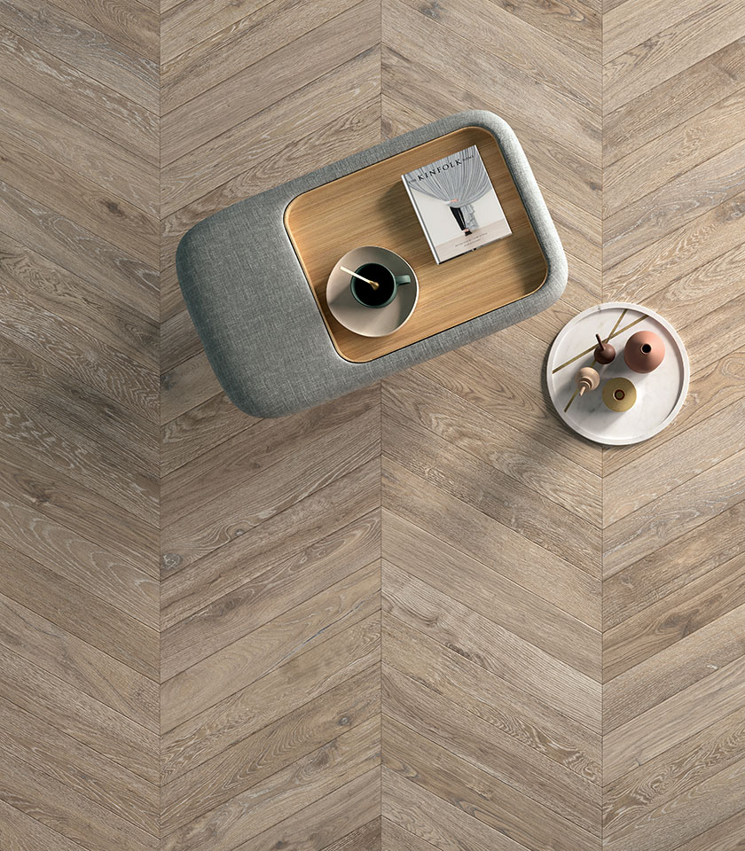 Wood-effect porcelain stoneware flooring laid in a chevron pattern, viewed from above with contemporary designer tables.